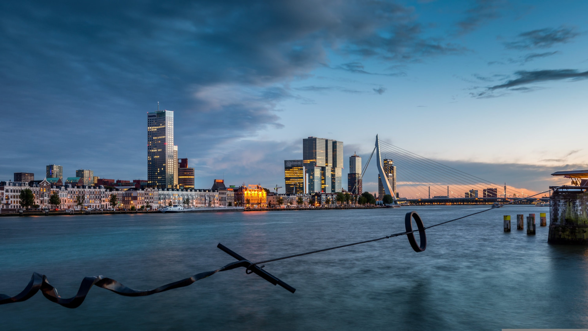 Skyline van Rotterdam bij schemering met de Erasmusbrug en lichtreflecties op het water